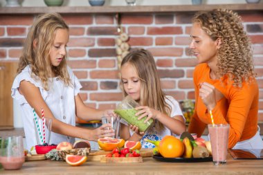 Anne ve kızları mutfakta birlikte yemek pişiriyorlar. Sağlıklı gıda konsepti. Mutlu aile portresi ve taze meyve suyu..