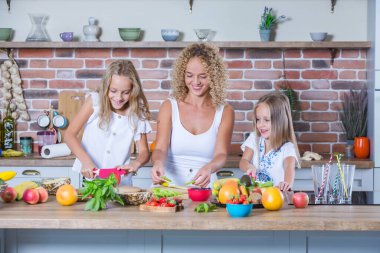 Anne ve kızları mutfakta birlikte yemek pişiriyorlar. Sağlıklı gıda konsepti. Mutlu aile portresi ve taze meyve suyu..