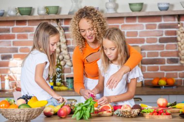 Anne ve kızları mutfakta birlikte yemek pişiriyorlar. Sağlıklı gıda konsepti. Mutlu aile portresi ve taze meyve suyu..