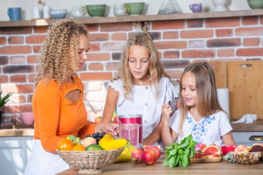Anne ve kızları mutfakta birlikte yemek pişiriyorlar. Sağlıklı gıda konsepti. Taze meyve suyu ile mutlu aile portresi. Mutlu kardeşler..