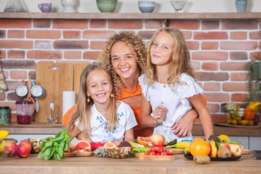 Anne ve kızları mutfakta birlikte yemek pişiriyorlar. Sağlıklı gıda konsepti. Taze meyve suyu ile mutlu aile portresi. Mutlu kardeşler..