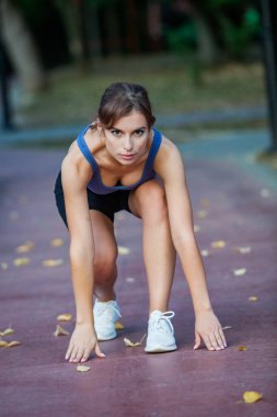Spor giyimli genç bir bayan dışarıda esneme egzersizleri yapıyor. Parkta spor yapan genç bir kızın portresi..