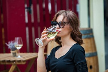 Güzel genç bir kadın bir restoranın terasında beyaz şarap içiyor. İşten sonra bir bardak şarapla dinleniyorum. Bekar kadın eğleniyor..