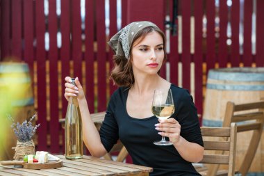 Güzel genç bir kadın bir restoranın terasında beyaz şarap içiyor. İşten sonra bir bardak şarapla dinleniyorum. Bekar kadın eğleniyor..