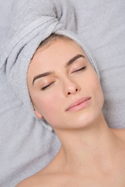 Портрет красивой молодой женщины с полотенцем на голове. Красивая молодая женщина получает массаж лица в спа-салоне. Косметические процедуры.