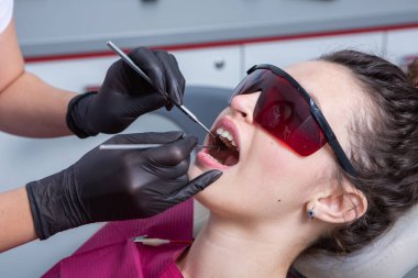 Güzel gülüşü olan genç bir bayan hasta dişçi kliniğinde diş muayenesi yapıyor. Sağlıklı dişler ve ilaçlar, stomatoloji konsepti