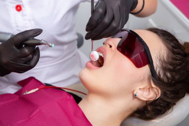 Güzel gülüşü olan genç bir bayan hasta dişçi kliniğinde diş muayenesi yapıyor. Sağlıklı dişler ve ilaçlar, stomatoloji konsepti