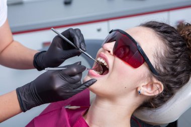 Dişçi, dişçi kliniğinde genç bir kadının dişlerini muayene ediyor. Dişçi konsepti. Diş hekimi ve hasta muayenehanesinde..