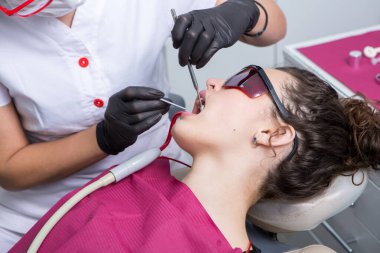 Dişçi, dişçi kliniğinde genç bir kadının dişlerini muayene ediyor. Dişçi konsepti. Diş hekimi ve hasta muayenehanesinde..