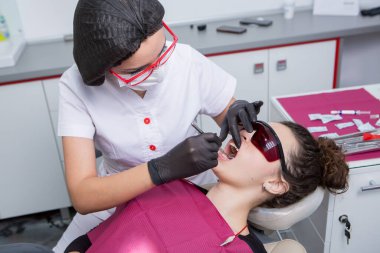 Dişçi, dişçi kliniğinde genç bir kadının dişlerini muayene ediyor. Dişçi konsepti. Diş hekimi ve hasta muayenehanesinde..