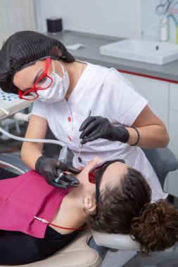 Dişçi, dişçi kliniğinde genç bir kadının dişlerini muayene ediyor. Dişçi konsepti. Diş hekimi ve hasta muayenehanesinde..