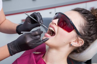 Stomatoloji ve diş bakımı. Diş hekimliği ve oral sağlık. Kadının dişçi kliniğinde diş muayenesi var. Yaklaş genç beyaz kız yüzü..