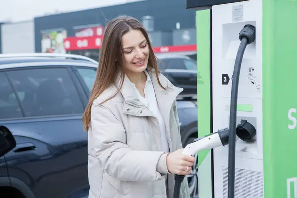 stock image Young woman charging her electric car at a charging station in the city. Eco fuel concept. The concept of environmentally friendly transport. Recharging battery from charging station.