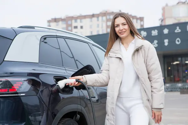 市内の充電ステーションで電気自動車を充電する若い女性 エコ燃料コンセプト 環境に優しい輸送の概念 充電ステーションからのバッテリーの充電 ロイヤリティフリーのストック写真