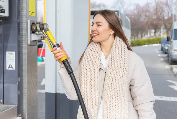 Young woman holding a fuel nozzle in her hand while refueling car at gas station. A stop for refueling at the gas station. Fueling the car with gas.