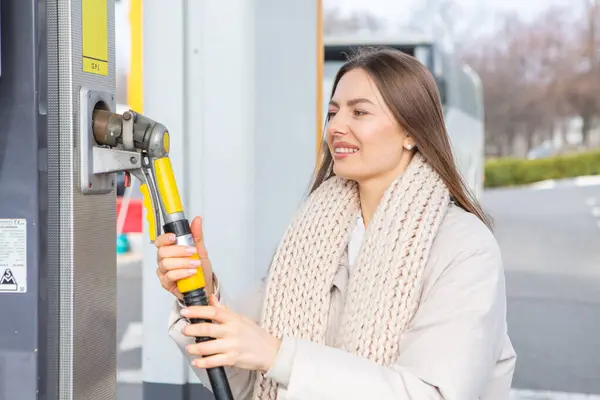 Young woman holding a fuel nozzle in her hand while refueling car at gas station. A stop for refueling at the gas station. Fueling the car with gas.