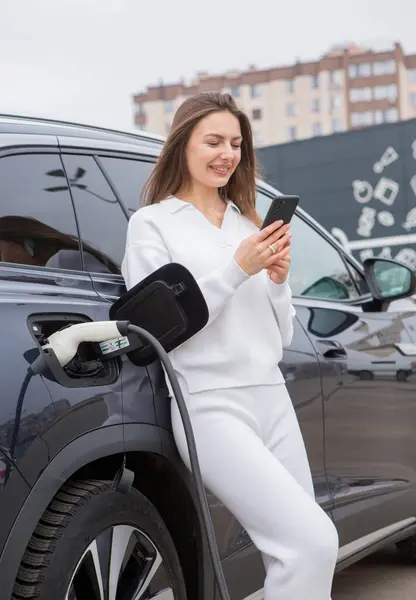 Young woman charging her electric car at a charging station in the city. Eco fuel concept. The concept of environmentally friendly transport. Recharging battery from charging station.