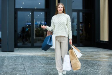Beyaz Avrupalı kadın alışveriş merkezinden dolu çantalarla çıkıyor. Güzel bir kadın alışveriş torbaları tutuyor..