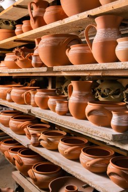 Çömlek atölyesindeki ahşap raflarda kuruyan taze kilden kupalar, çömlekler ve kaseler. El yapımı seramik imalatı. Atölyedeki farklı çömlekler. 