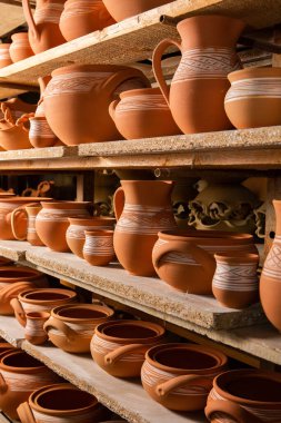 Çömlek atölyesindeki ahşap raflarda kuruyan taze kilden kupalar, çömlekler ve kaseler. El yapımı seramik imalatı. Atölyedeki farklı çömlekler. 