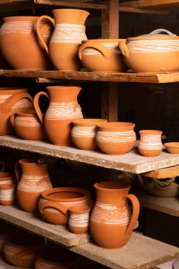 Çömlek atölyesindeki ahşap raflarda kuruyan taze kilden kupalar, çömlekler ve kaseler. El yapımı seramik imalatı. Atölyedeki farklı çömlekler. 