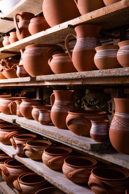 Çömlek atölyesindeki ahşap raflarda kuruyan taze kilden kupalar, çömlekler ve kaseler. El yapımı seramik imalatı. Atölyedeki farklı çömlekler. 