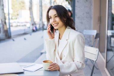 Şehirdeki modern bir kafede genç bir blogcu ya da nüfuzlu biri telefonda konuşuyor. Beyaz ceketli genç bir iş kadını..