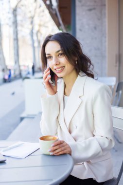 Şehirdeki modern bir kafede genç bir blogcu ya da nüfuzlu biri telefonda konuşuyor. Beyaz ceketli genç bir iş kadını..