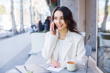 Şehirdeki modern bir kafede genç bir blogcu ya da nüfuzlu biri telefonda konuşuyor. Beyaz ceketli genç bir iş kadını..