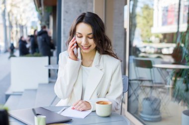 Şehirdeki modern bir kafede genç bir blogcu ya da nüfuzlu biri telefonda konuşuyor. Beyaz ceketli genç bir iş kadını..