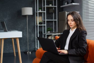 Ofiste kanepede otururken dizüstü bilgisayarda çalışan güzel bir iş kadını.