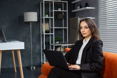Ofiste kanepede otururken dizüstü bilgisayarda çalışan güzel bir iş kadını.