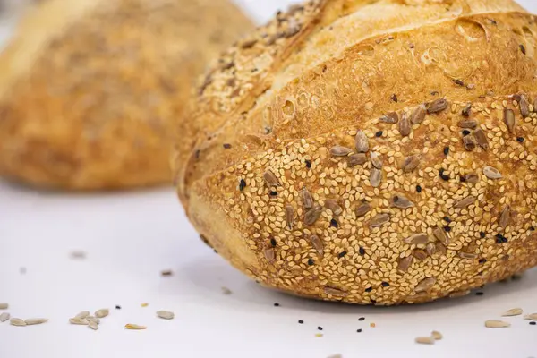 Beyaz zemin üzerinde susamlı ve ayçiçeği tohumlu tam bir buğday ekmeği.