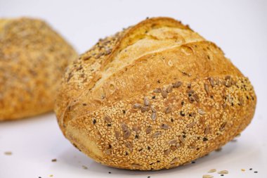 Beyaz zemin üzerinde susamlı ve ayçiçeği tohumlu tam bir buğday ekmeği.