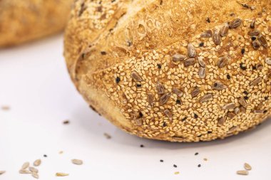 Beyaz zemin üzerinde susamlı ve ayçiçeği tohumlu tam bir buğday ekmeği.