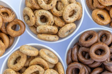 Koyu arkaplanda yeni pişmiş mini simit. Üst Manzara. Yüzük şeklinde krakerler, yakın plan. Küçük ekmek çemberi bisküvisi. Farklı simit türleri olan kaseler..