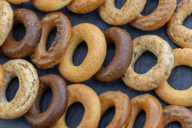 Koyu arkaplanda yeni pişmiş mini simit. Üst Manzara. Yüzük şeklinde krakerler, yakın plan. Küçük ekmek çemberi bisküvisi. Farklı simit türleri olan kaseler..
