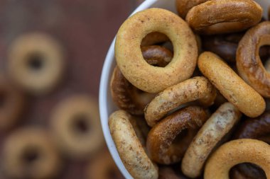 Koyu arkaplanda yeni pişmiş mini simit. Üst Manzara. Yüzük şeklinde krakerler, yakın plan. Küçük ekmek çemberi bisküvisi. Farklı simit türleri olan kaseler..