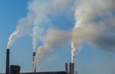 Fabrika bacalarından mavi gökyüzüne doğru yükselen endüstriyel kirlilik. Ekolojik felaket. Fabrika bacaları dumanla dolu.