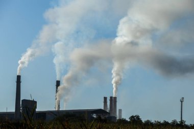 Fabrika bacalarından mavi gökyüzüne doğru yükselen endüstriyel kirlilik. Ekolojik felaket. Fabrika bacaları dumanla dolu.