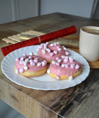 Bir fincan limonlu siyah çay ve ahşap bir masada pembe kremalı üç çörek. Tatlı kahvaltı..