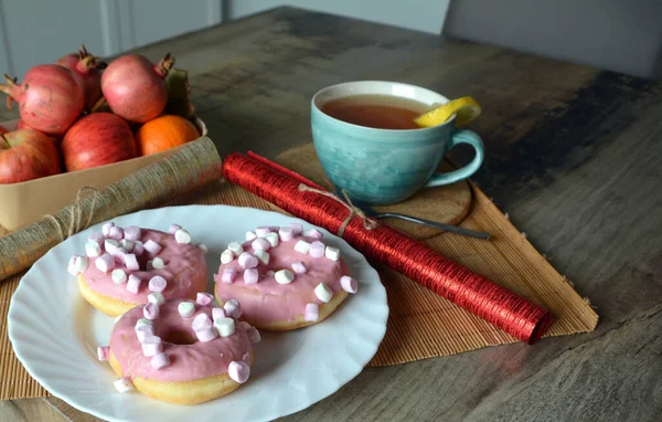 Bir fincan limonlu siyah çay ve ahşap bir masada pembe kremalı üç çörek. Tatlı kahvaltı..