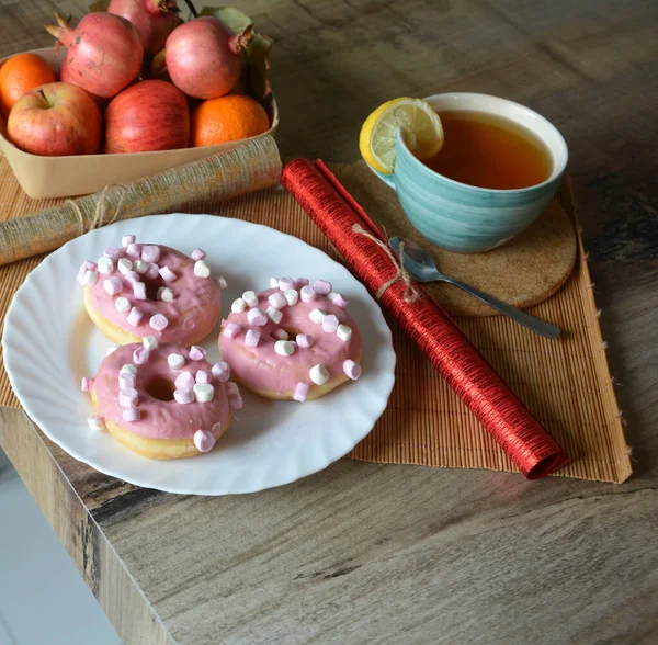 Bir fincan limonlu siyah çay ve ahşap bir masada pembe kremalı üç çörek. Tatlı kahvaltı..