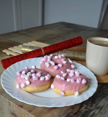 Sütlü bir fincan kahve ve beyaz tabakta pembe kremalı üç çörek. Tatlı kahvaltı.. 