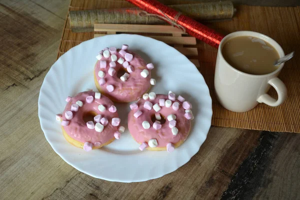 Sütlü bir fincan kahve ve beyaz tabakta pembe kremalı üç çörek. Tatlı kahvaltı.. 