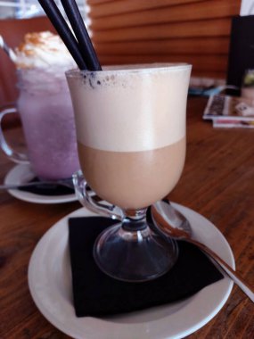 Tahta bir masada çırpılmış sütle bir bardak buzlu kahve..