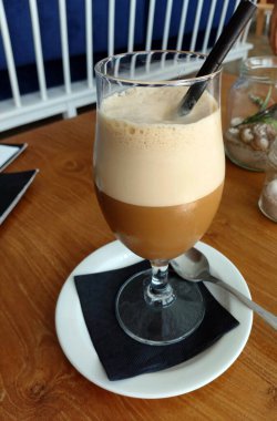 Tahta bir masada çırpılmış sütle bir bardak buzlu kahve..