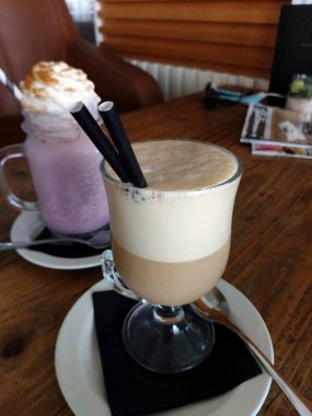 Tahta bir masada çırpılmış sütle bir bardak buzlu kahve..