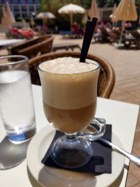 Tahta bir masada çırpılmış sütle bir bardak buzlu kahve..