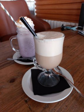 Tahta bir masada çırpılmış sütle bir bardak buzlu kahve..